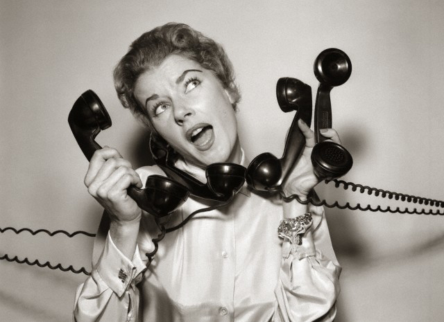 1950 --- 1950s 1960s Overwhelmed Stressed Woman Answering Four Black Telephone Phone Receivers At One Time --- Image by © DeBrocke/ClassicStock/Corbis